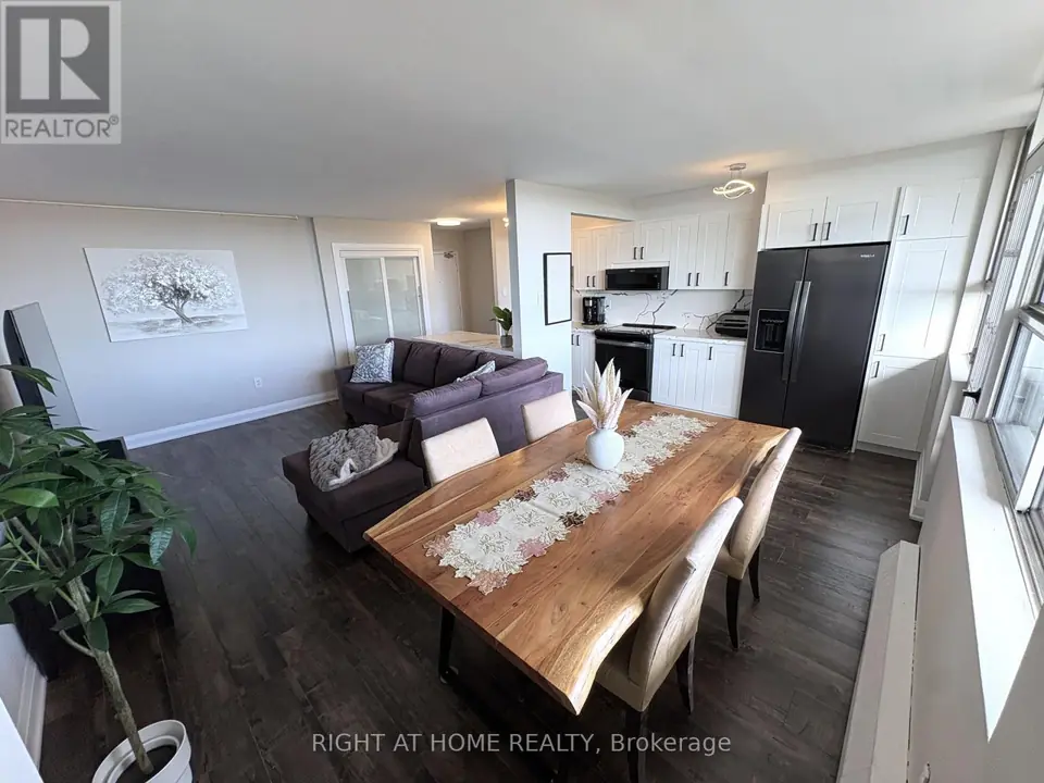 Wide elevated view of open-plan room with dining table, purple sectional sofa, white kitchen and hallway sliding doors.
